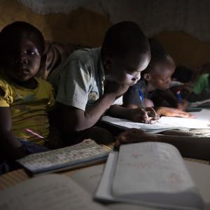 A group of children gathered around books, using a flashlight to read more clearly.