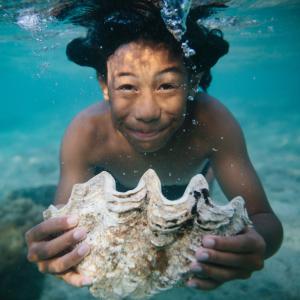Boy swimming under water with a large sea shell. 
