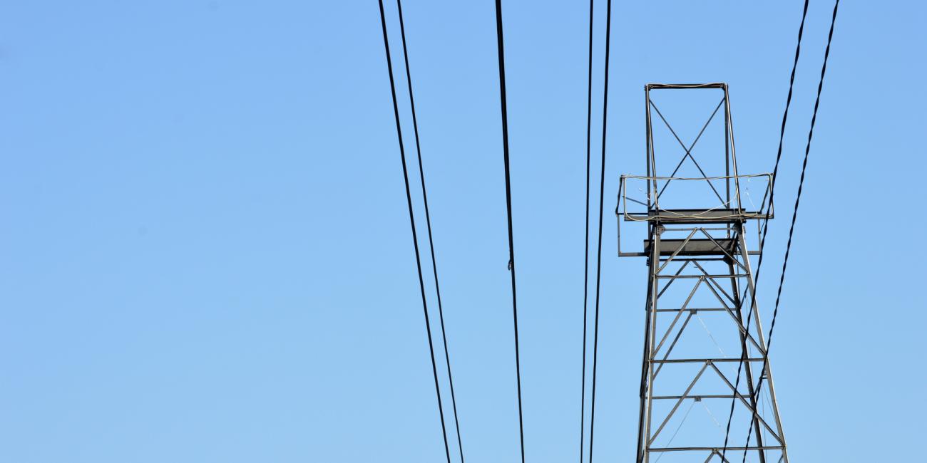 A power line and metal power pole with a clear blue sky as a background.