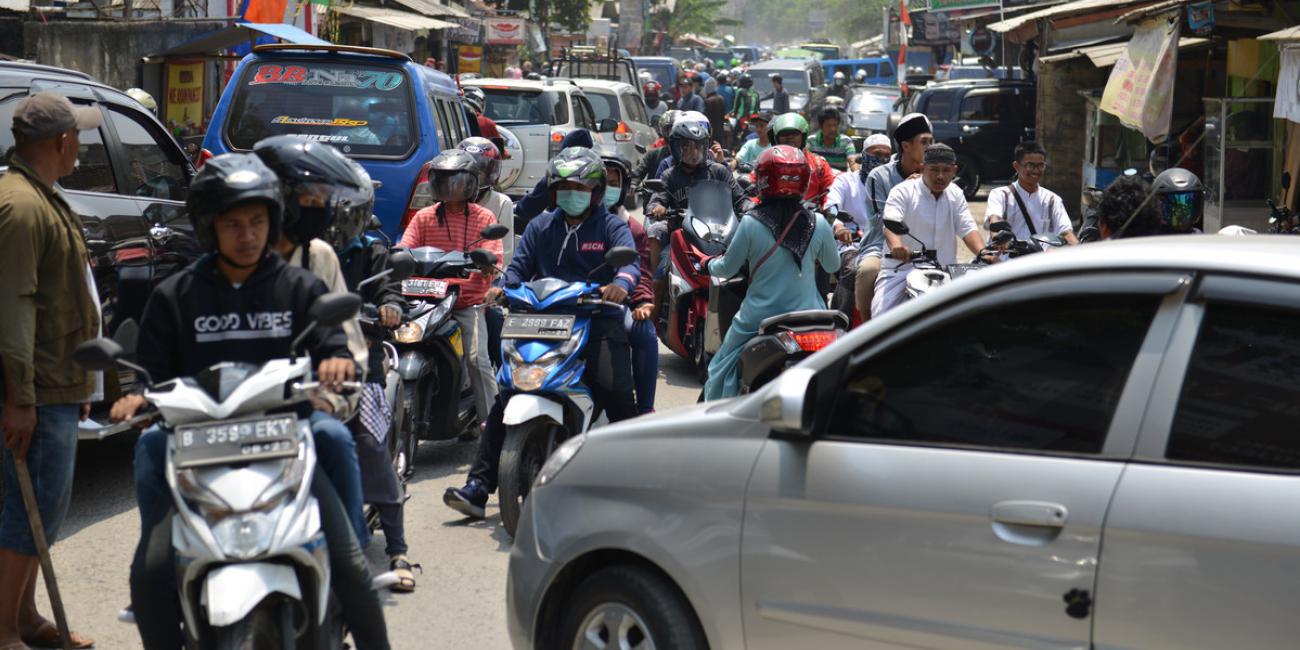 Men and women on motorcycles in a busy urban street in Jakarta, Indonesia, with some wearing face masks to protect from viruses and pollution.