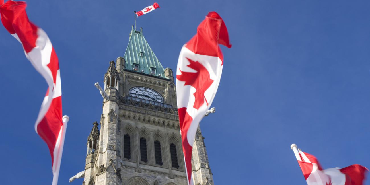 The Peace Tower of Canada's Parliament-building-stands between two Canadian flags.