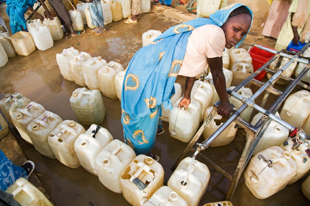 Woman at a water point in Sudan picking up canisters of water