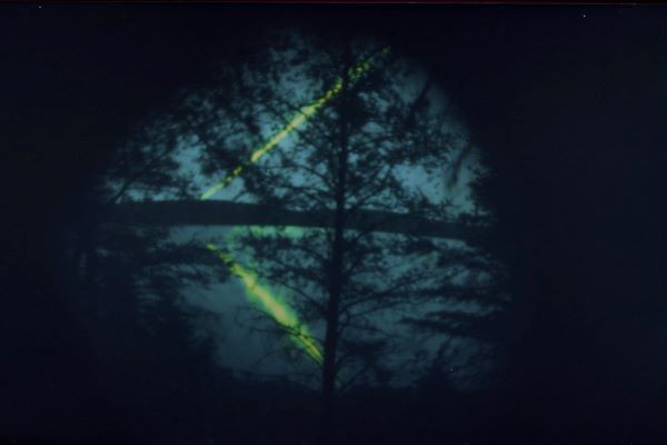 Dark image of lake and trees with beam of green light