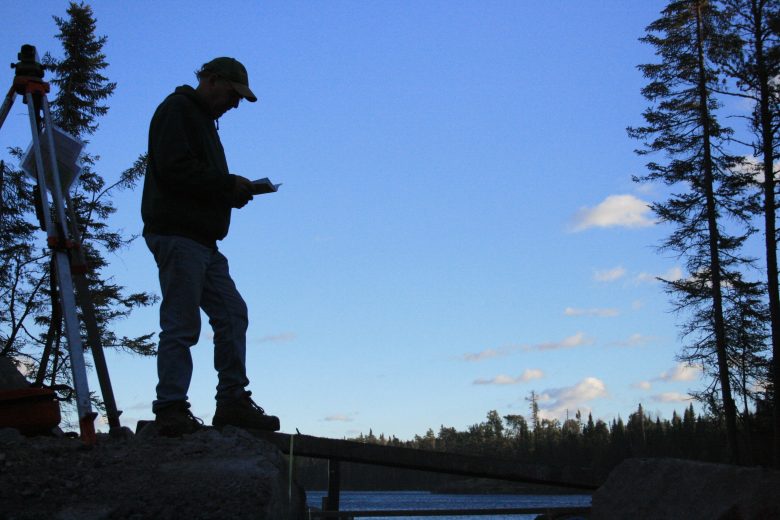 Silhouette of a man standing beside a lake taking notes
