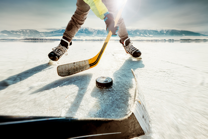 person playing pond hockey about to hit a puck in front of some mountains.