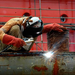 A worker wears a mask while he is welding in a bright red industrial background.
