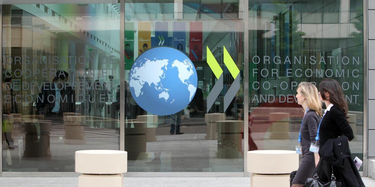 Two women walking in front of a building with the OECD logo. 