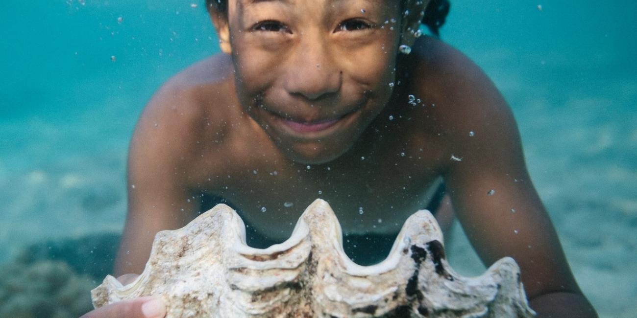 Boy swimming under water with a large sea shell. 