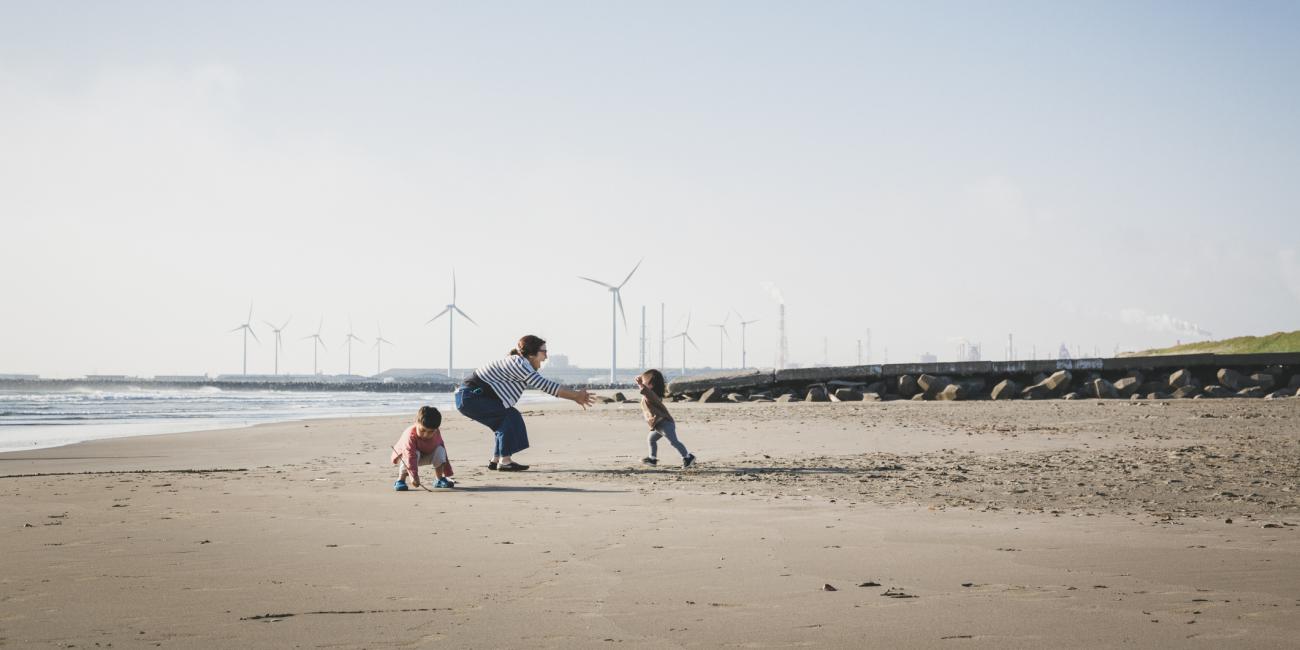 Mother and children playing on a beach with wind turbines in the background