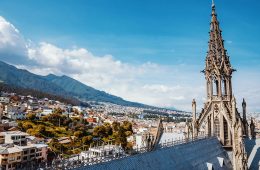 A church tower overlooks city buildings surrounded by mountains.