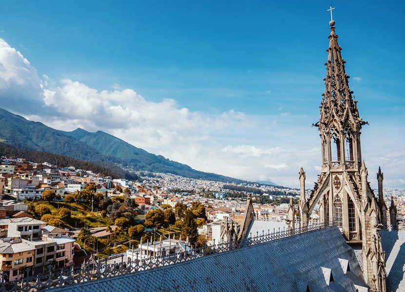 A church tower overlooks city buildings surrounded by mountains.