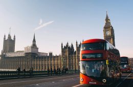 A red double-decker bus passes a palace in a city.
