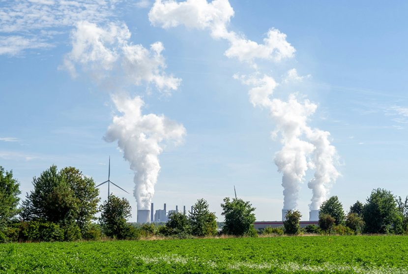 A power plant and wind turbines operate near a green field.