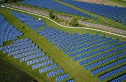 Solar panels line a grass field next to a highway.
