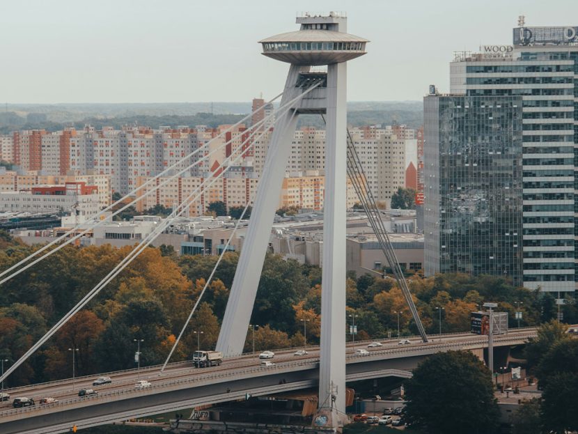 Cars travel along a massive bridge with city buildings in the background.