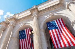 Two American flags hang from a building.