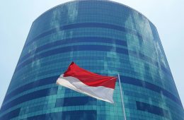 The flag of Indonesia flies in front of a tall, glass building.