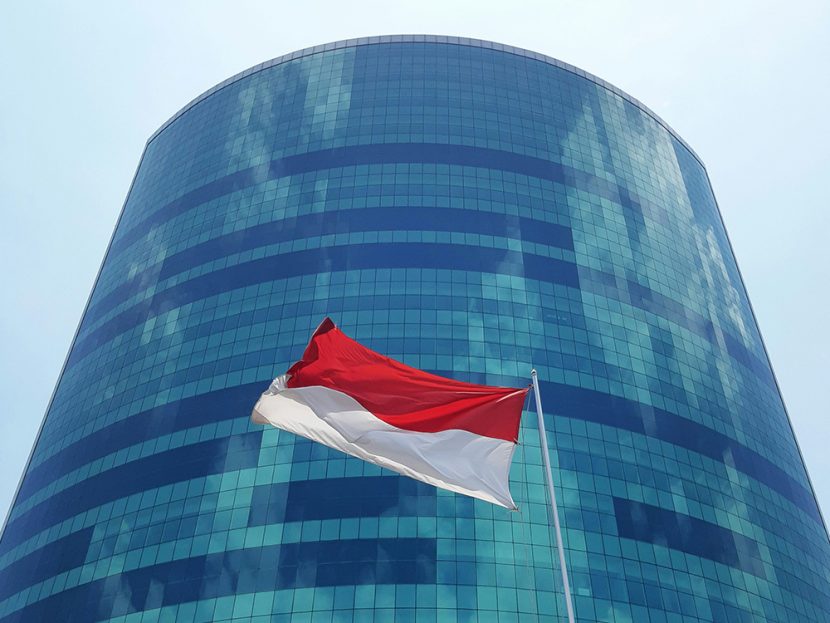 The flag of Indonesia flies in front of a tall, glass building.