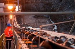 A miner inspects ore rocks moving along a conveyor belt at a site in Australia.