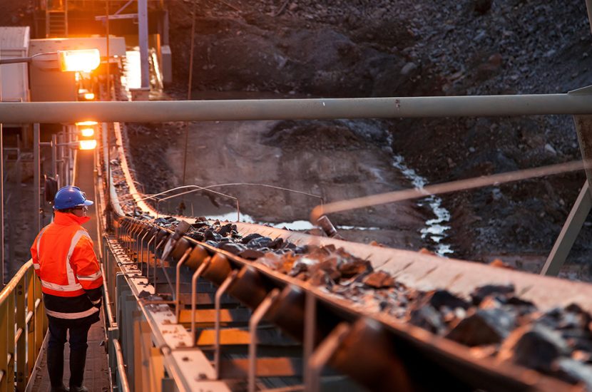 A miner inspects ore rocks moving along a conveyor belt at a site in Australia.