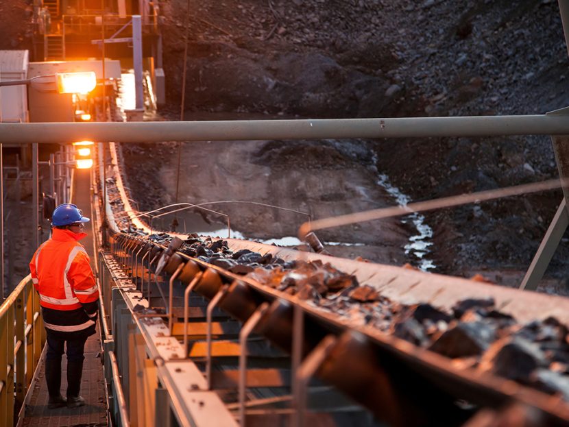A miner inspects ore rocks moving along a conveyor belt at a site in Australia.
