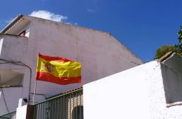 The flag of Spain flies in front of a building.
