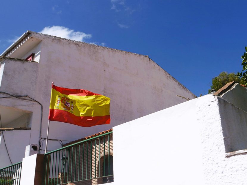 The flag of Spain flies in front of a building.