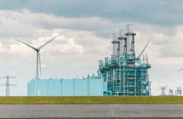 Wind turbines next to an industrial plant.