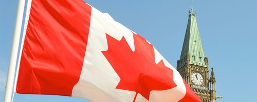 The red-and-white Canada flag flies in front of a government building.