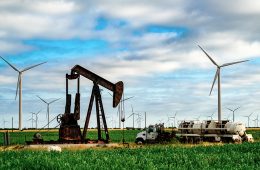 An oil pump surrounded by wind turbines.