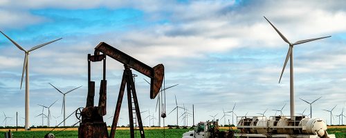 An oil pump surrounded by wind turbines.