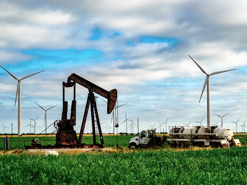 An oil pump surrounded by wind turbines.
