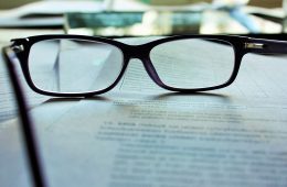 A pair of eye glasses sit on a stack of paper.