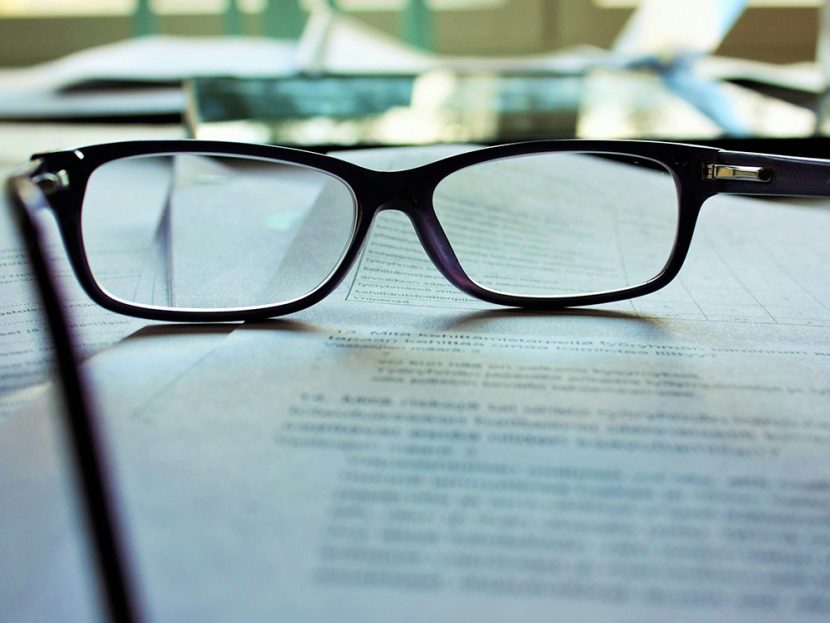 A pair of eye glasses sit on a stack of paper.