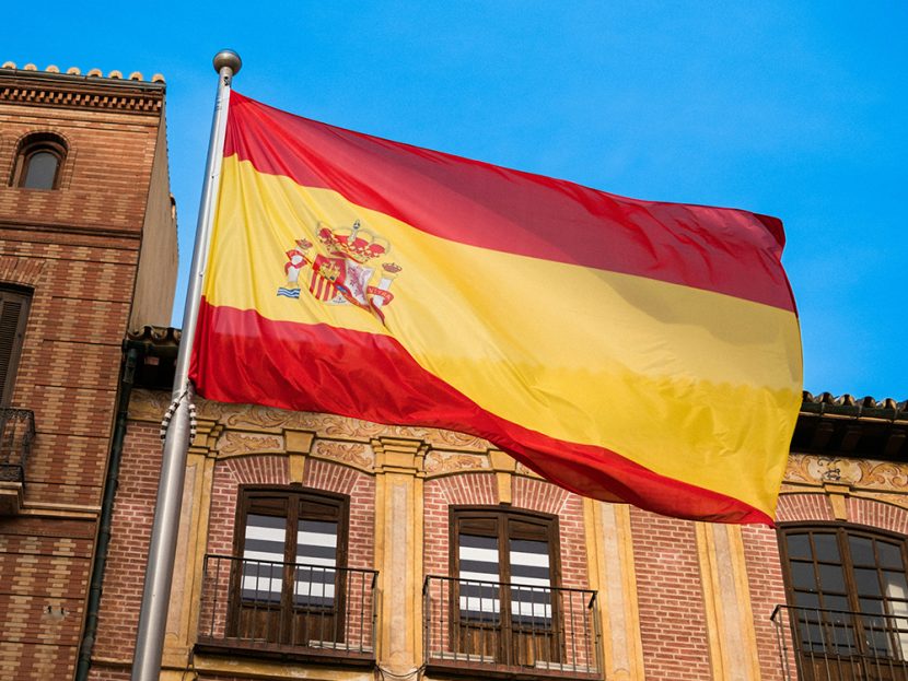 A red-and-yellow flag flies in front of a brown building.