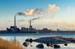 Stacks emit exhaust in an industrial area on a waterfront.
