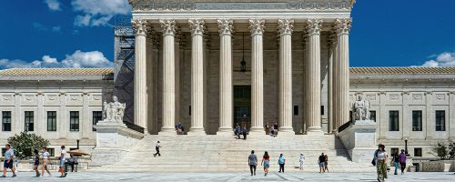 People pass by a grand white building.