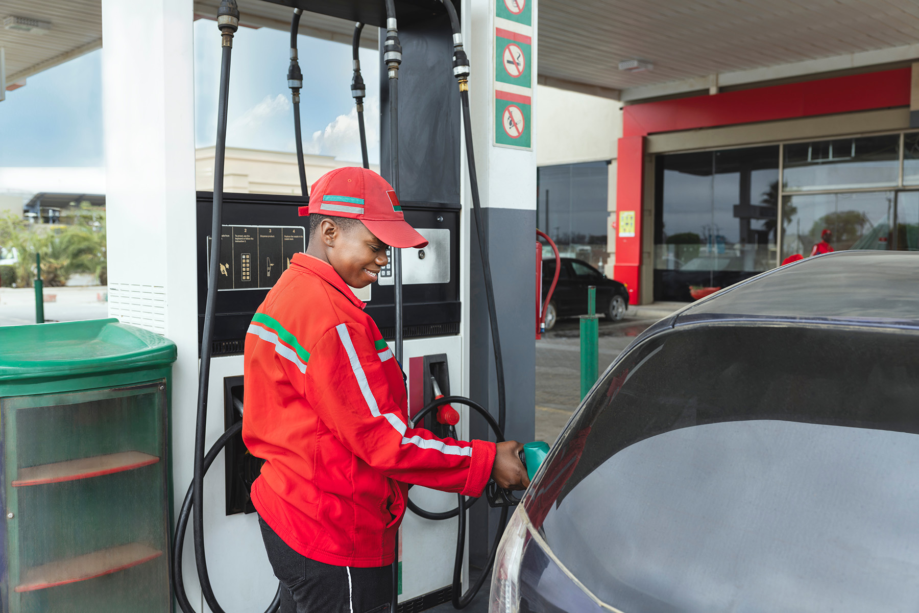 Black gas attendant in red coat pumps gas at a gas station