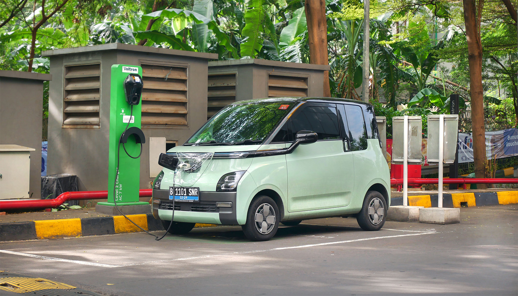Electric wuling car charging at EV charging station with lush tropical greenery in the background.