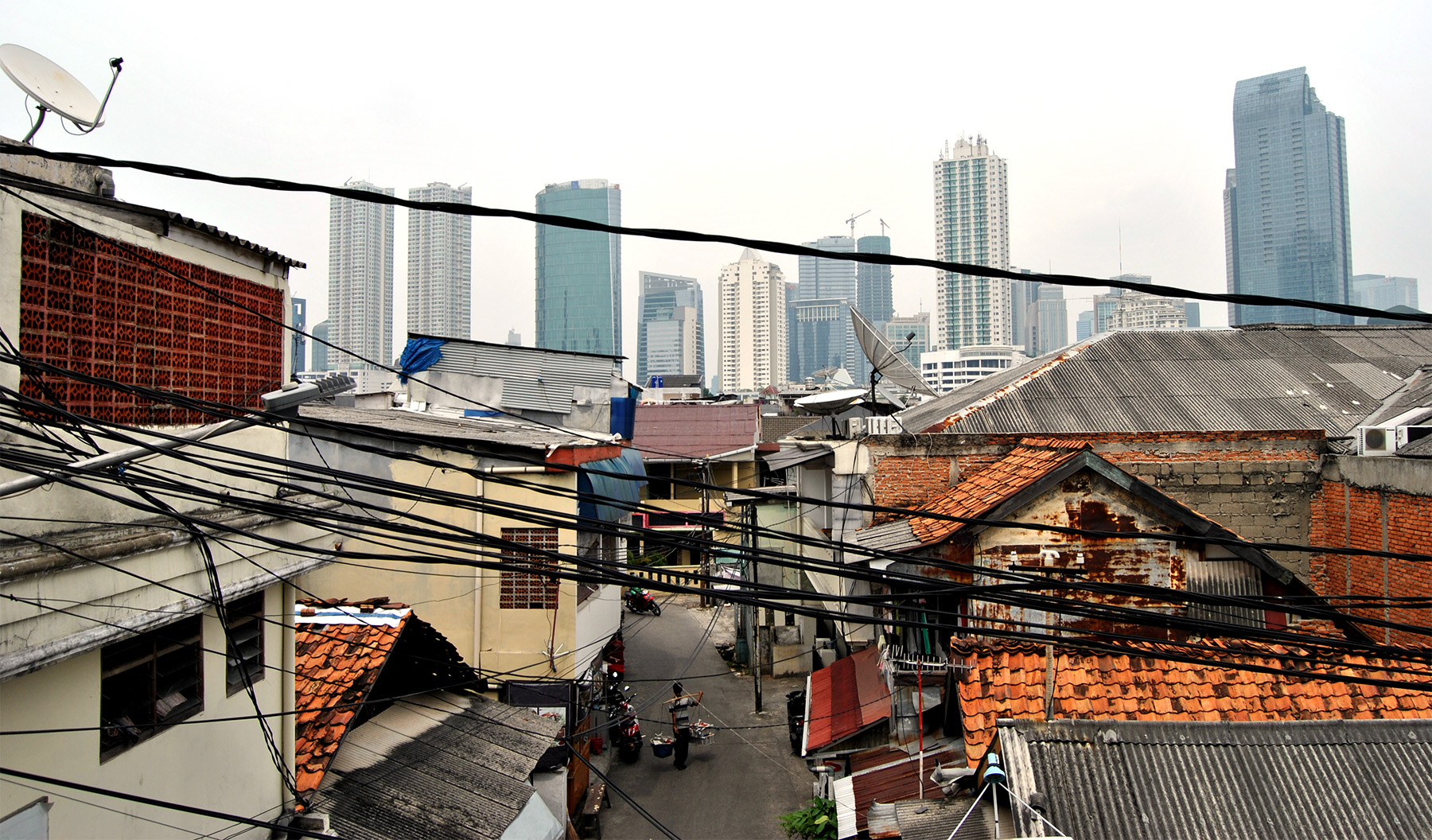 Power lines strung between old houses with skyscrapers in the background.