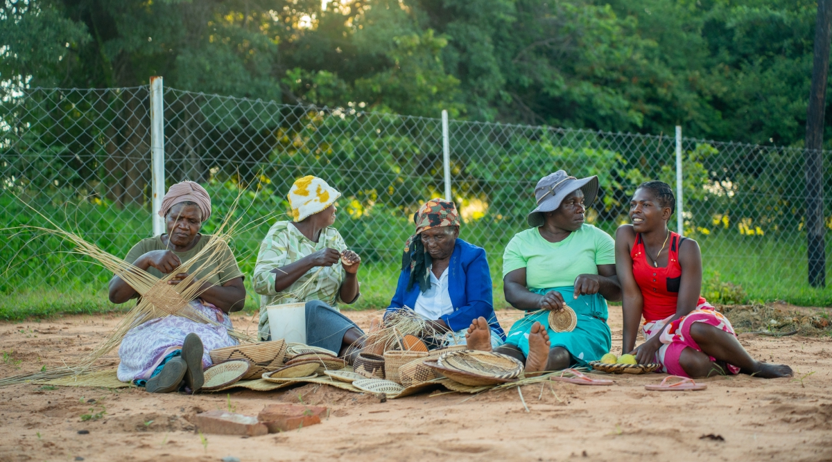 5 women seated weaving with ilala