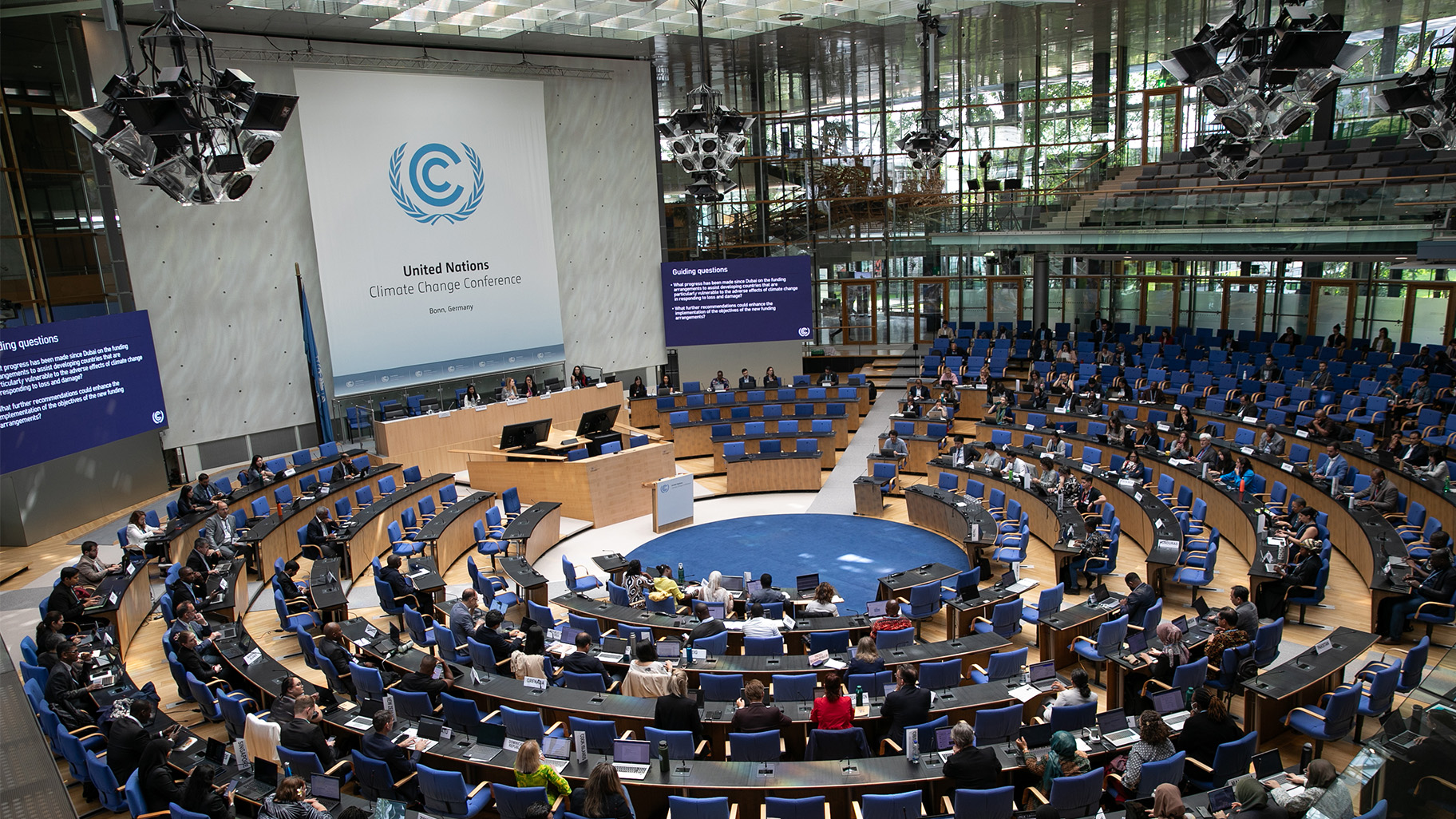 Climate negotiators sit at long tables that curve around a circular UN conference room.