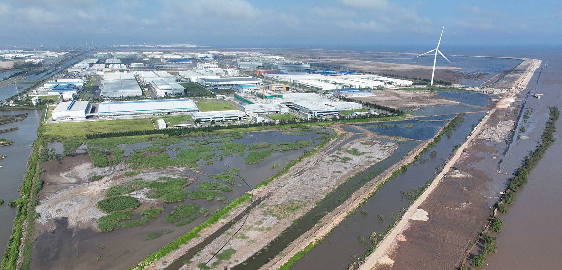 Aerial view of buildings next to a coastal wetland with a wind turbine in the background.