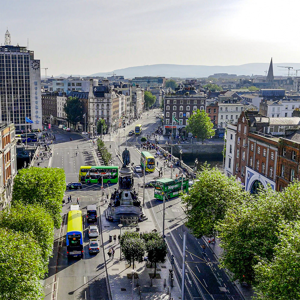 High-angled view looking down wide boulevard with monument in the centre and buses and cars on the road.