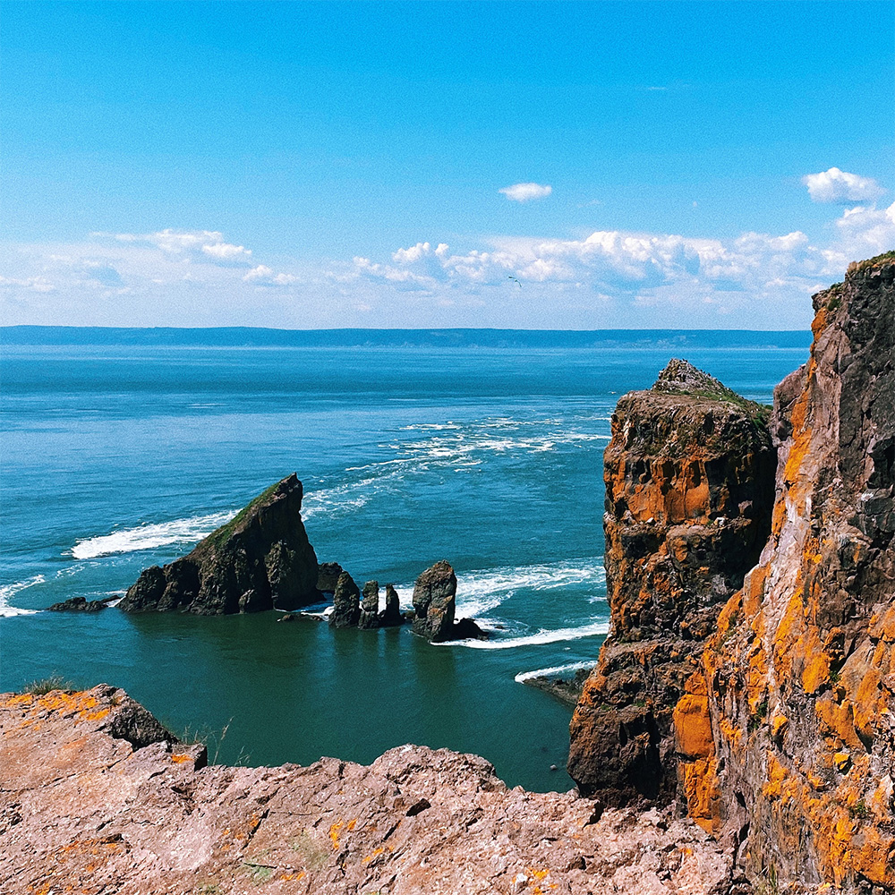 Cliffs with red lichen on the right, next to the sea with a grey rock jutting out in the left.
