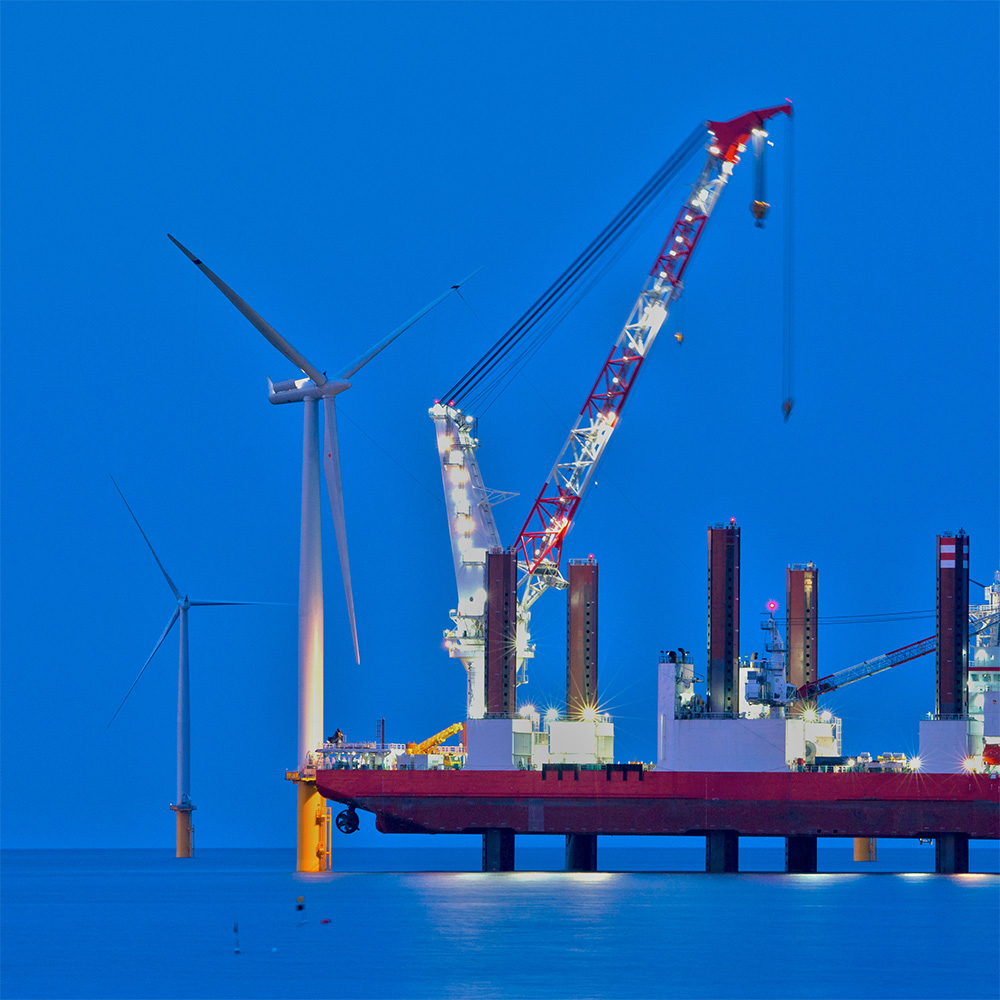 Offshore oil rig at dusk with wind turbines behind.