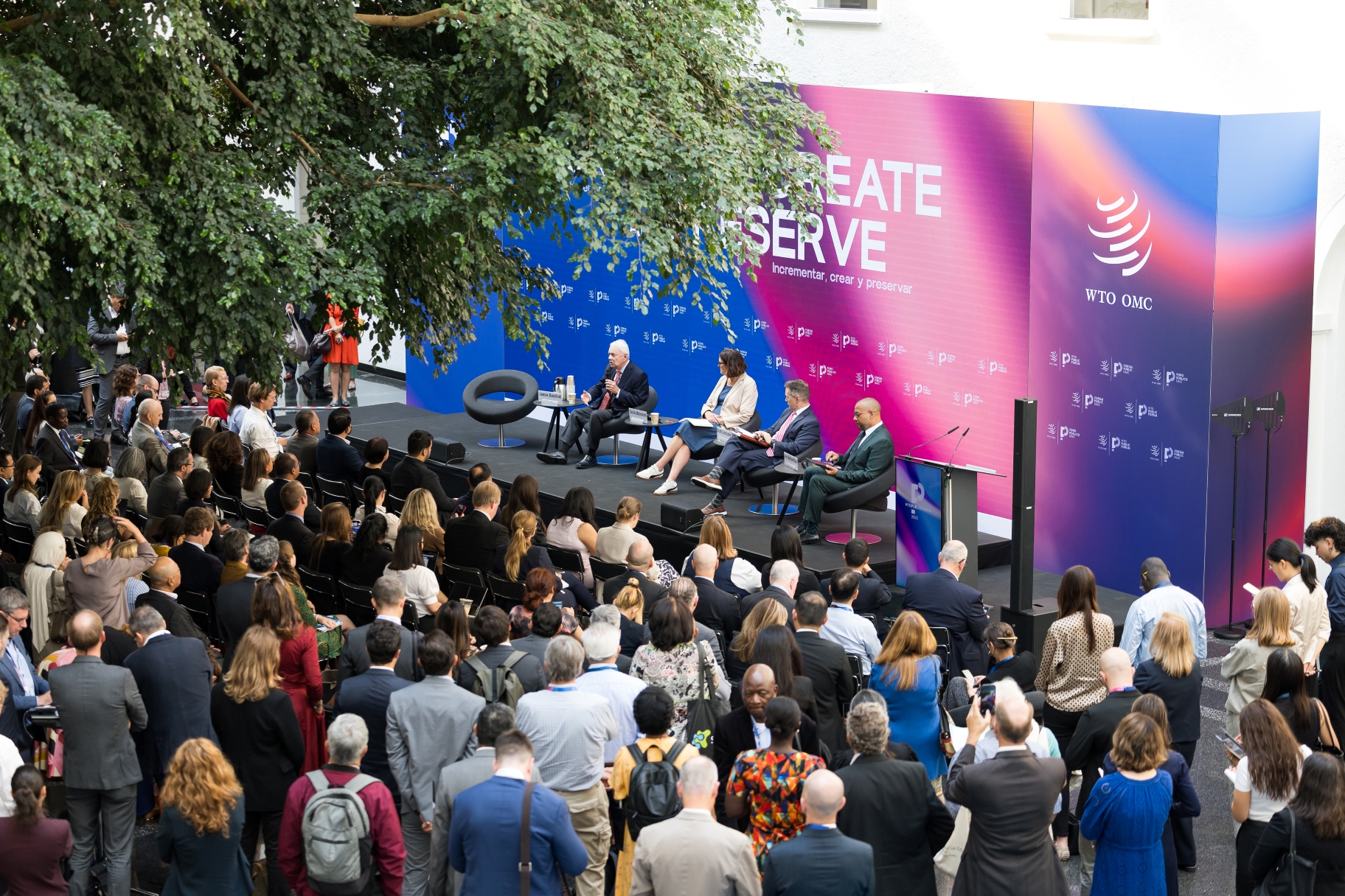 People sit in an atrium, watching speakers on stage in front of a colourful banner.
