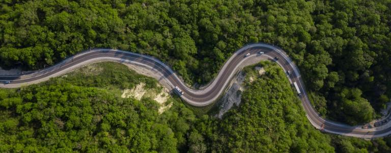 A bird's eye view of a two-lane highway curving through a green forest