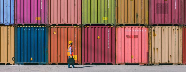 A man in construction vest walks by rows of colourful shipping containers