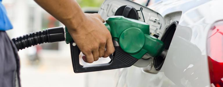 A hand filling a car with gas using a green nozzle